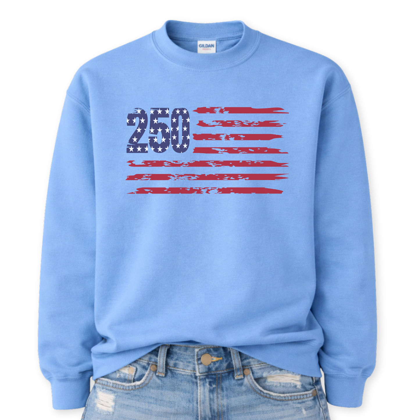 Gildan Carolina Blue crewneck sweatshirt mockup with a front tuck into distressed denim, featuring a bold “250” star-filled graphic with distressed red flag stripes forming a patriotic American flag design.