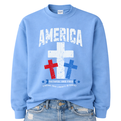 Christian patriotic faith graphic on a blue sweatshirt. The design features a bold distressed “America” arch across the chest with a large central white cross, flanked by red and blue crosses below for a strong USA color story. A banner reading “Faithful and Free” anchors the design, with smaller text noting “Finding True Liberty in Christ,” blending faith-forward messaging with classic Fourth of July patriotic style.