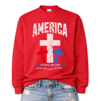 Christian patriotic faith graphic on a red sweatshirt. The design features a bold distressed “America” arch across the chest with a large central white cross, flanked by red and blue crosses below for a strong USA color story. A banner reading “Faithful and Free” anchors the design, with smaller text noting “Finding True Liberty in Christ,” blending faith-forward messaging with classic Fourth of July patriotic style.