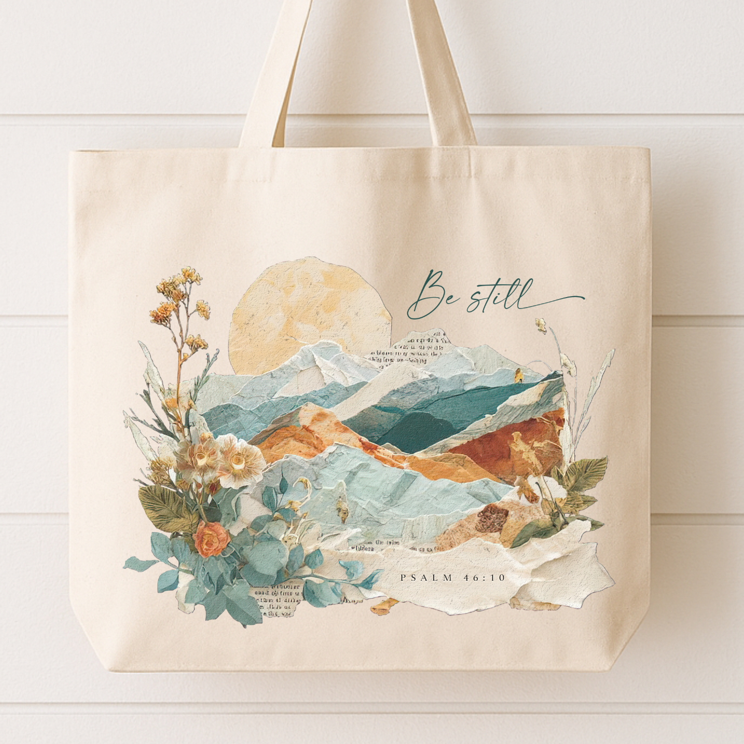 Tote bag with mountain and floral design and 'Be still' text on a white background