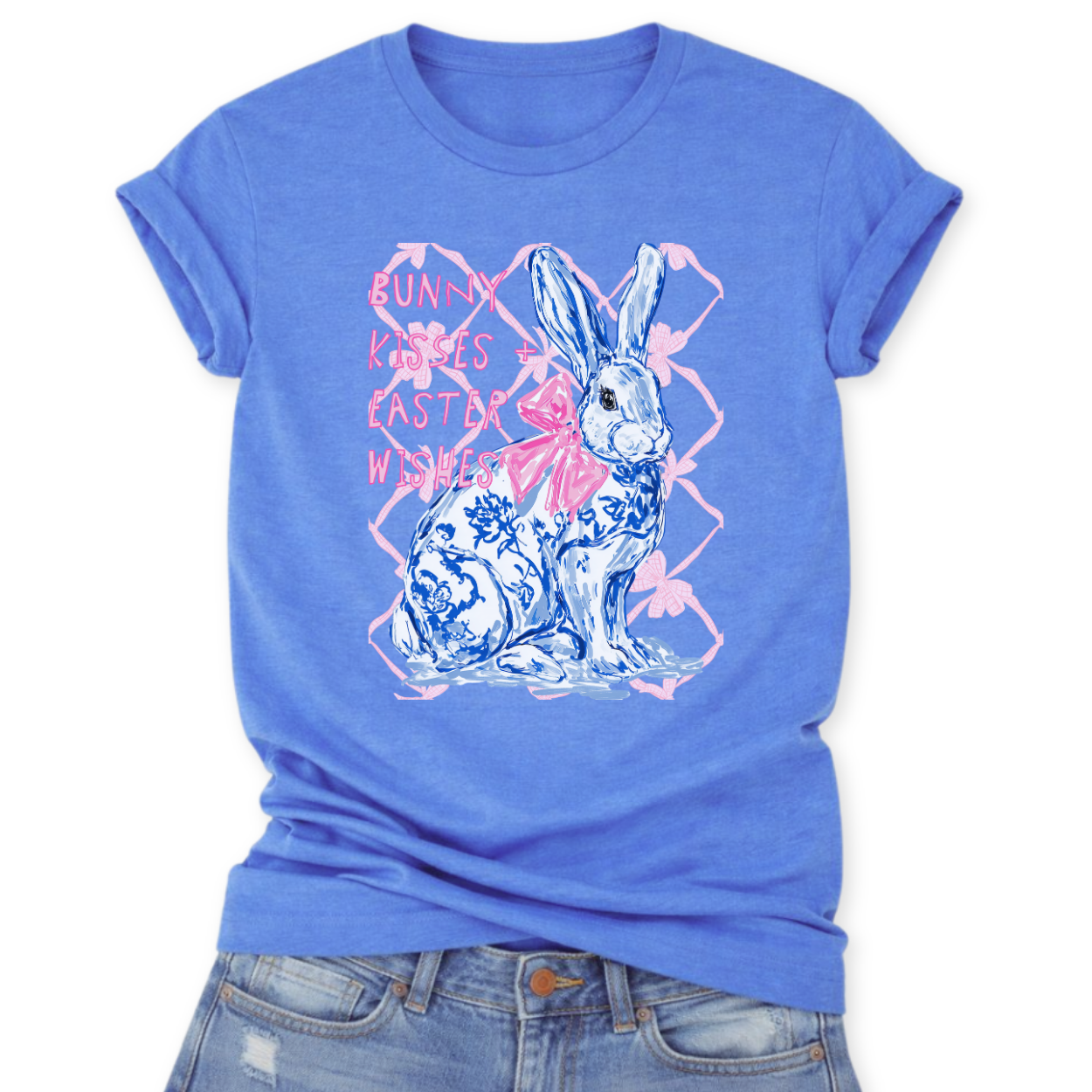 Easter spring graphic on a Bella Canvas t-shirt. The design features a hand-illustrated bunny in blue toile-style floral detailing, accented with a soft pink bow and layered over a subtle bow-pattern background. The phrase “Bunny Kisses + Easter Wishes” appears in playful pastel lettering, blending classic spring charm with boutique-ready styling.
