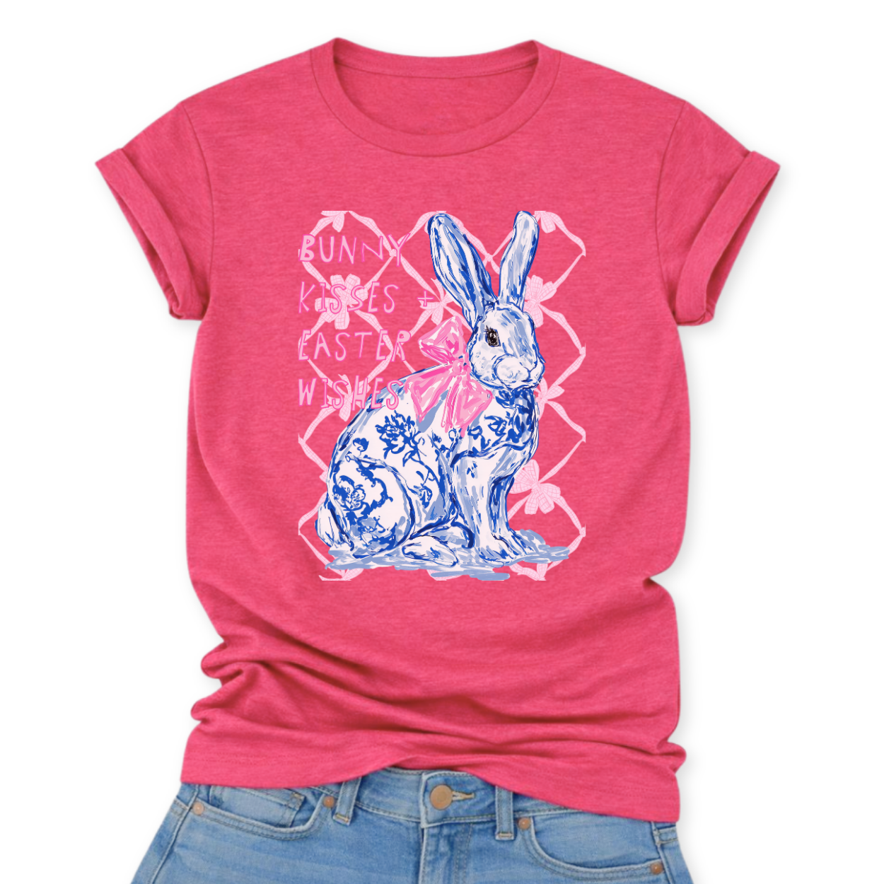 Easter spring graphic on a Bella Canvas t-shirt. The design features a hand-illustrated bunny in blue toile-style floral detailing, accented with a soft pink bow and layered over a subtle bow-pattern background. The phrase “Bunny Kisses + Easter Wishes” appears in playful pastel lettering, blending classic spring charm with boutique-ready styling.