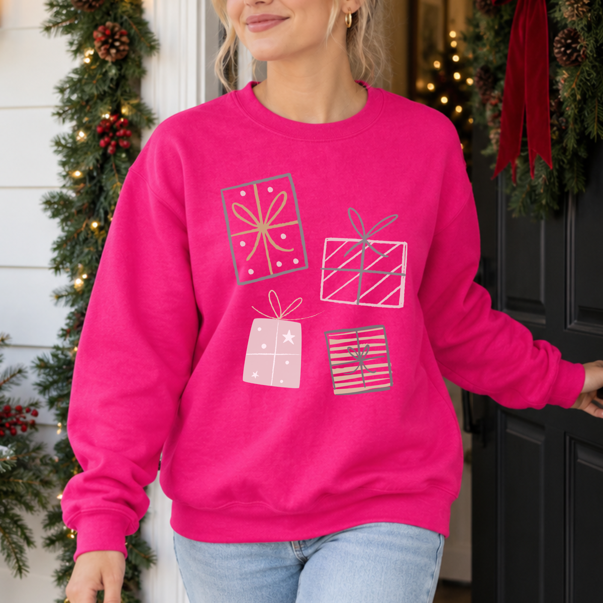 A festive Christmas graphic featuring stacked presents in soft gray, pink, and gold tones on a heliconia pink sweatshirt