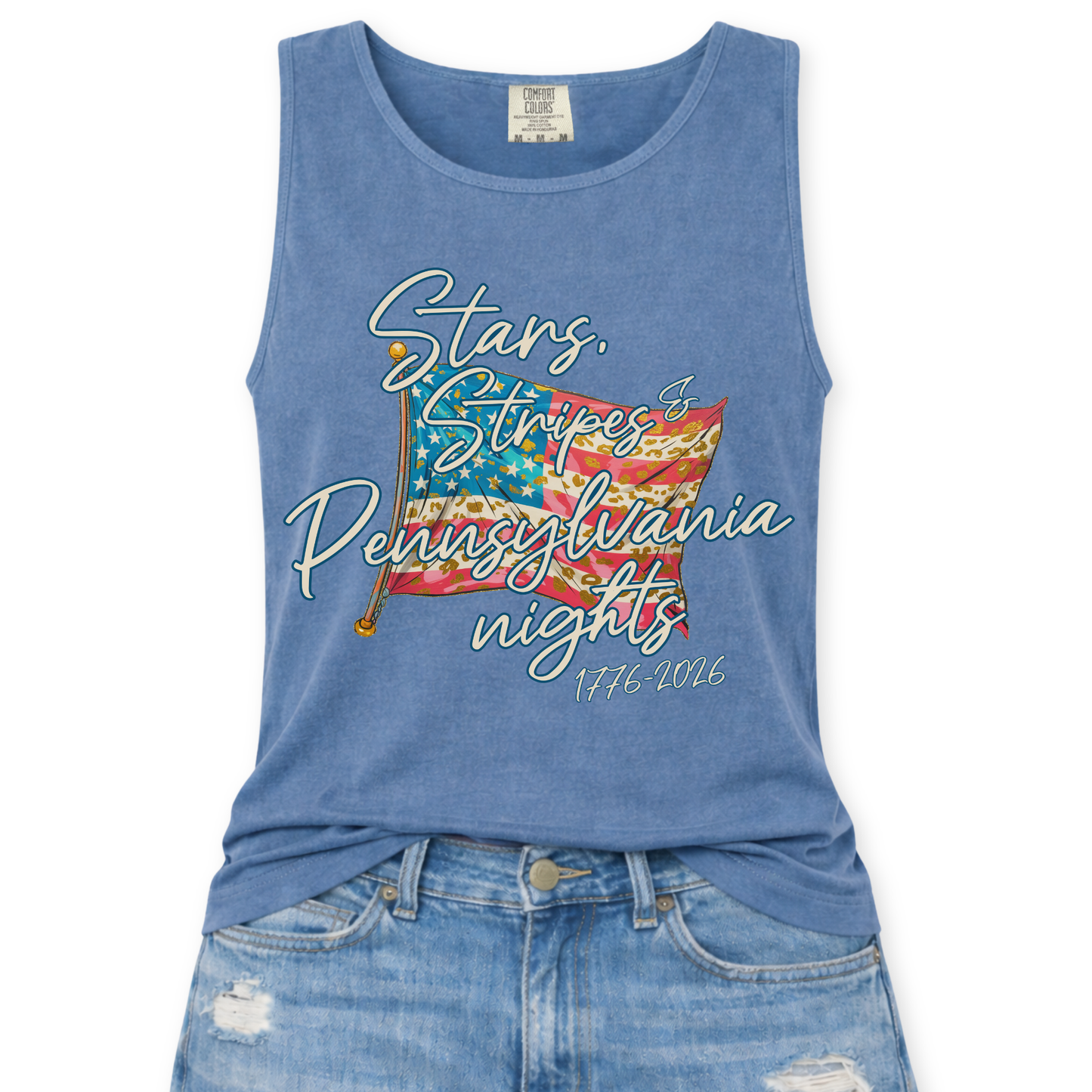 Blue Jean Comfort Colors tank top featuring a patriotic American flag graphic with mixed stripe patterns and script text reading “Stars, Stripes & Indiana nights” with “1776–2026” underneath, styled with light wash denim jeans.