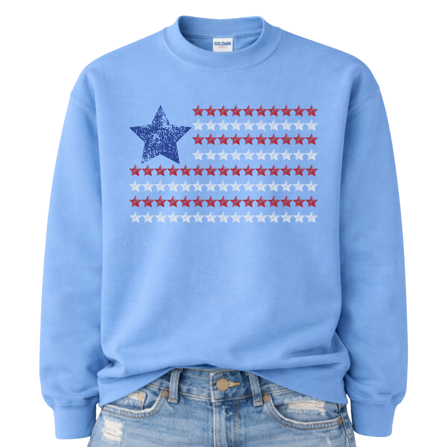 Patriotic Americana flag graphic on a blue sweatshirt. The design features a distressed blue star at the top left with horizontal rows of red stars creating a flag-inspired layout. The worn, vintage texture gives it an easy Americana look while staying clean and bold for everyday wear. A simple patriotic staple for Fourth of July, summer holidays, and USA-themed seasonal collections.