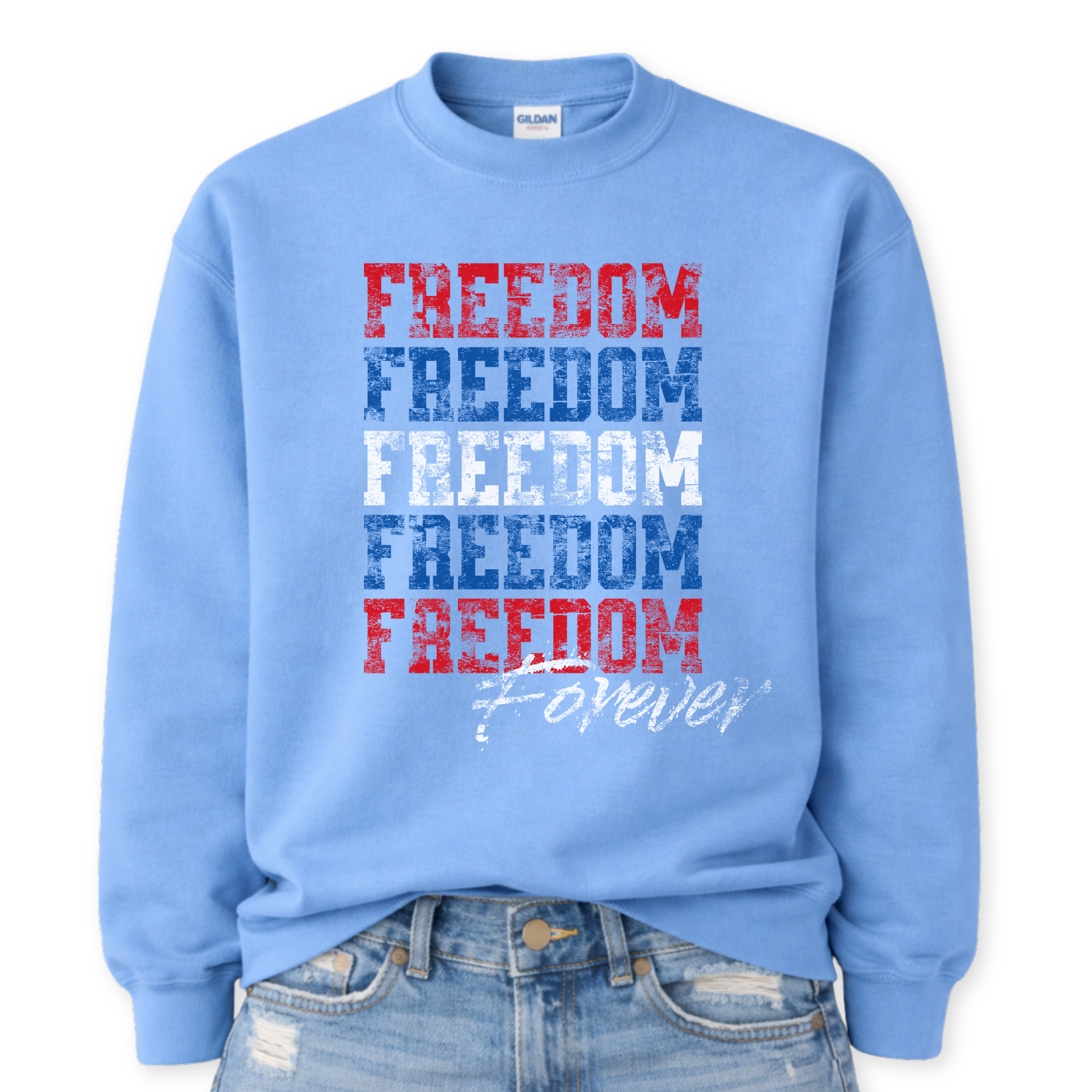 Gildan Carolina Blue crewneck sweatshirt mockup with front tuck into distressed jeans, featuring stacked distressed “FREEDOM” text in red, blue, and white with a “Forever” script at the bottom.