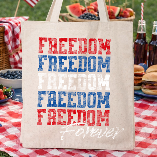 Patriotic Fourth of July freedom quote graphic on a 100% cotton canvas tote bag. The design features bold “FREEDOM” lettering printed in red, white, and blue with a coordinating “Forever” script accent, creating a clean Americana statement piece for July 4th seasonal merchandising and patriotic gift assortments.

