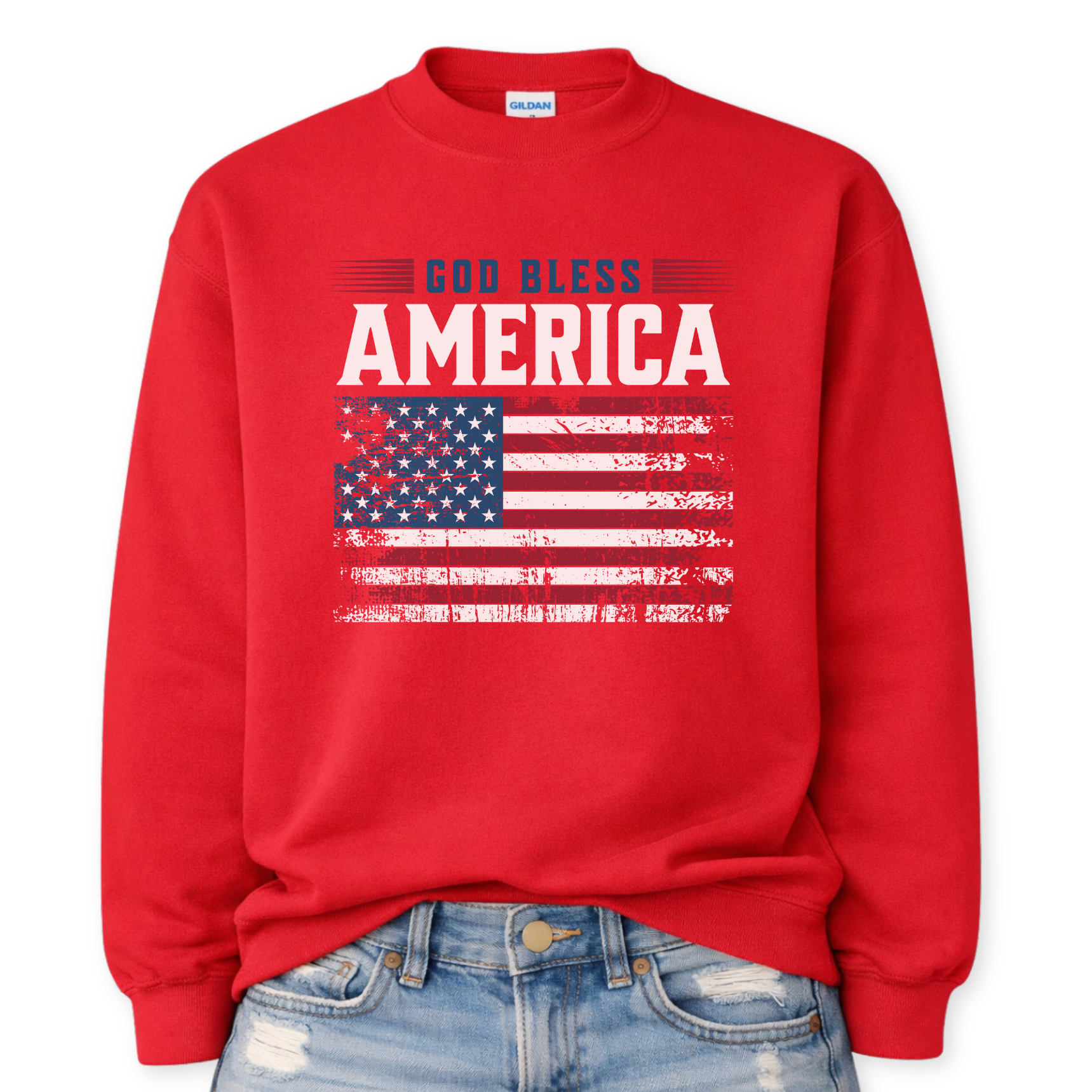 Gildan red crewneck sweatshirt mockup with a front tuck into distressed denim, featuring “GOD BLESS” above large “AMERICA” and a distressed American flag graphic on the front.