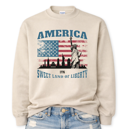 Beige sweatshirt with American flag and Statue of Liberty design on a white background.  America, 1776 Sweet Land Of Liberty saying