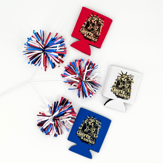 Assorted collapsible can coolers in red, white, and royal blue displayed with red, white, and blue metallic pom poms. The graphic features a distressed Statue of Liberty design with bold wording that reads “Liberty Justice” printed on the front of the drink sleeve style can coolers.