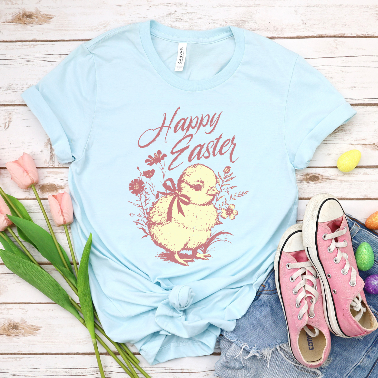 Heather Baby Blue Easter seasonal graphic on a Bella Canvas t-shirt. The design features a vintage-inspired illustration of two children dressed in bunny outfits gathered around a rabbit with pastel Easter eggs and soft greenery. The phrase “May the gifts of Easter bring you hope that grows” curves above the artwork in delicate script lettering, creating a nostalgic, heartfelt spring message.