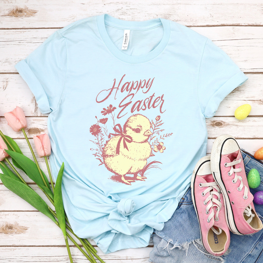 Heather Baby Blue Easter seasonal graphic on a Bella Canvas t-shirt. The design features a vintage-inspired illustration of two children dressed in bunny outfits gathered around a rabbit with pastel Easter eggs and soft greenery. The phrase “May the gifts of Easter bring you hope that grows” curves above the artwork in delicate script lettering, creating a nostalgic, heartfelt spring message.