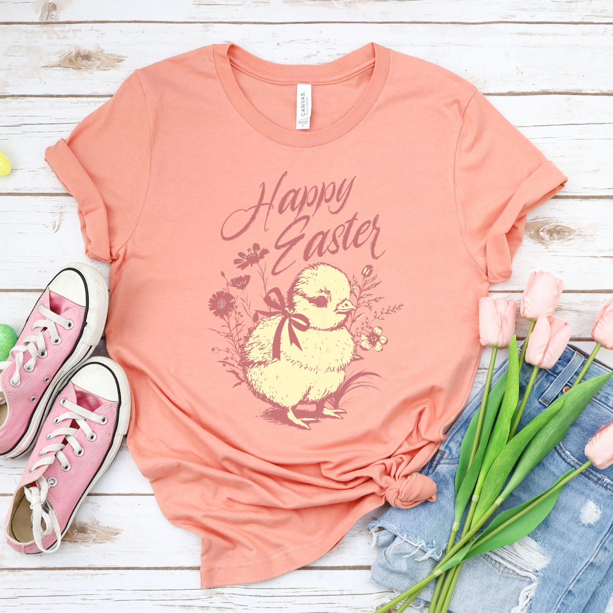 Heather Sunset Easter seasonal graphic on a Bella Canvas t-shirt. The design features a vintage-inspired illustration of two children dressed in bunny outfits gathered around a rabbit with pastel Easter eggs and soft greenery. The phrase “May the gifts of Easter bring you hope that grows” curves above the artwork in delicate script lettering, creating a nostalgic, heartfelt spring message.