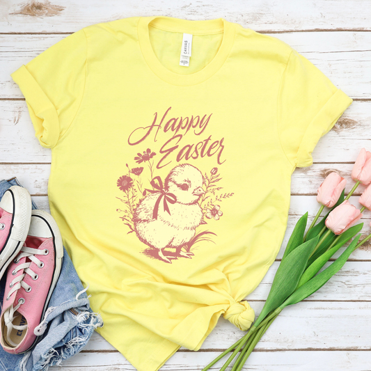 Heather Yellow Easter seasonal graphic on a Bella Canvas t-shirt. The design features a vintage-inspired illustration of two children dressed in bunny outfits gathered around a rabbit with pastel Easter eggs and soft greenery. The phrase “May the gifts of Easter bring you hope that grows” curves above the artwork in delicate script lettering, creating a nostalgic, heartfelt spring message.