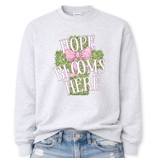 Gray sweatshirt with 'Hope Blooms Here' text and pink bow design on a white background