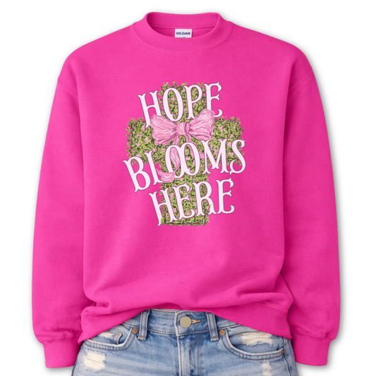 Pink sweatshirt with 'Hope Blooms Here' text and floral design on a white background