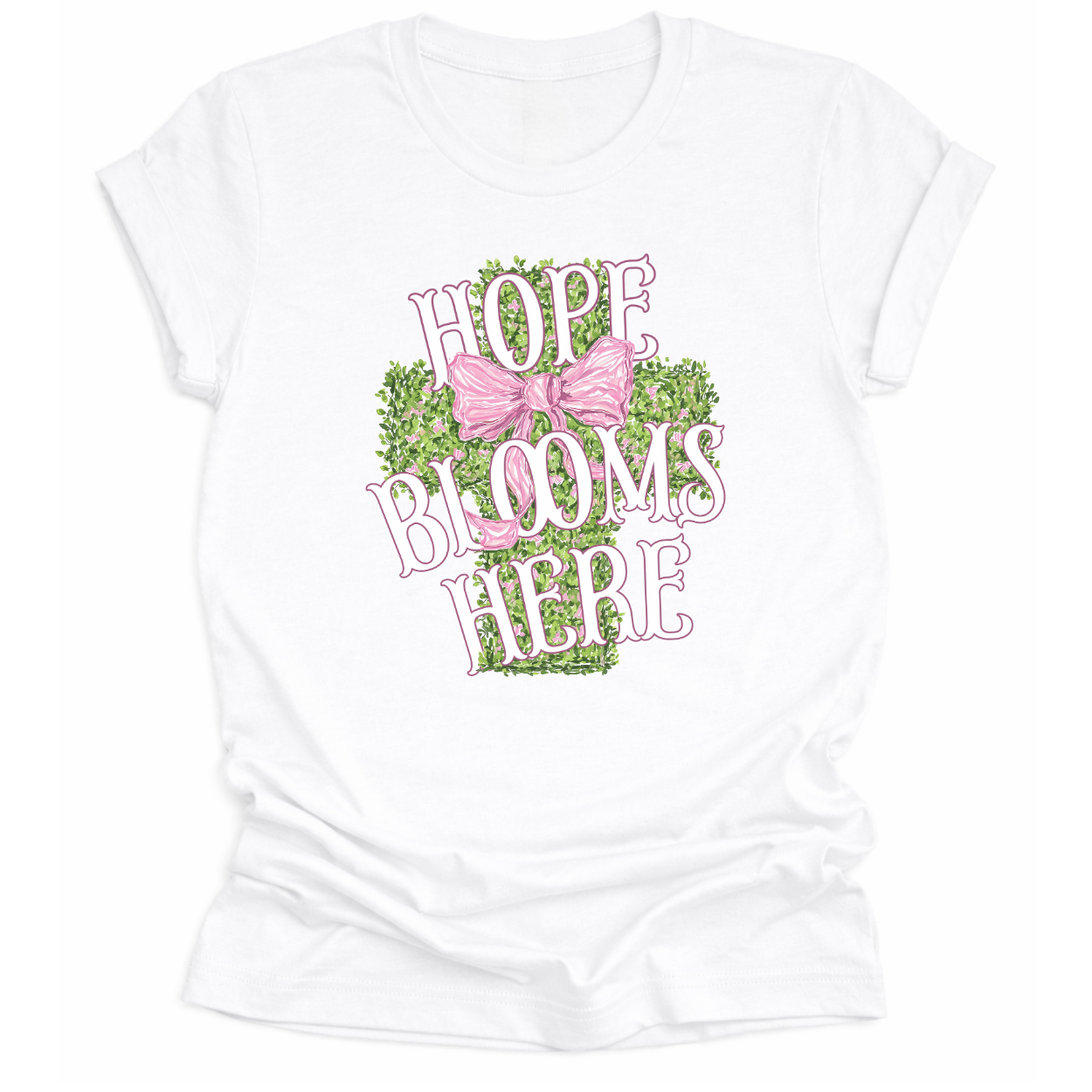 Christian spring cross graphic on a Bella Canvas t-shirt. The design features a greenery-filled cross adorned with a large pink bow, layered with the phrase “Hope Blooms Here” in bold, vintage-inspired lettering. The artwork blends Easter symbolism with soft feminine styling, creating a faith-forward seasonal piece.&nbsp;