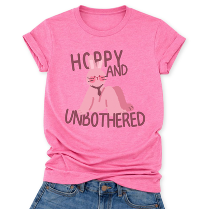 Heather Charity Pink Playful Easter graphic on a Bella Canvas t-shirt. The design features a relaxed pink bunny illustration paired with the bold phrase “Hoppy and Unbothered” in modern, oversized lettering. The artwork blends trendy humor with soft seasonal styling, making it a fun spring statement piece.