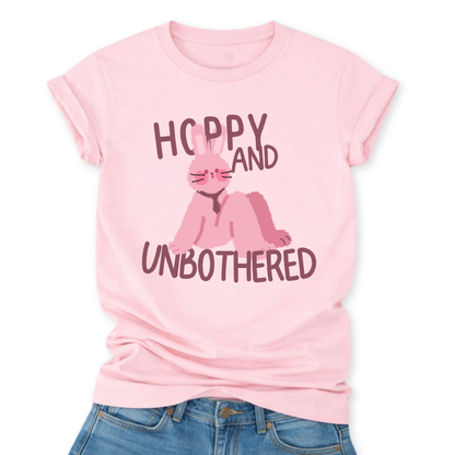 Heather Pink Playful Easter graphic on a Bella Canvas t-shirt. The design features a relaxed pink bunny illustration paired with the bold phrase “Hoppy and Unbothered” in modern, oversized lettering. The artwork blends trendy humor with soft seasonal styling, making it a fun spring statement piece.