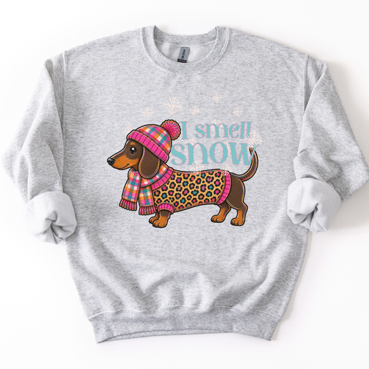 I smell snow featuring a dachshund dog bundled up in a sweater and hat with snowflakes around him.  On a ash gray heliconia sweatshirt