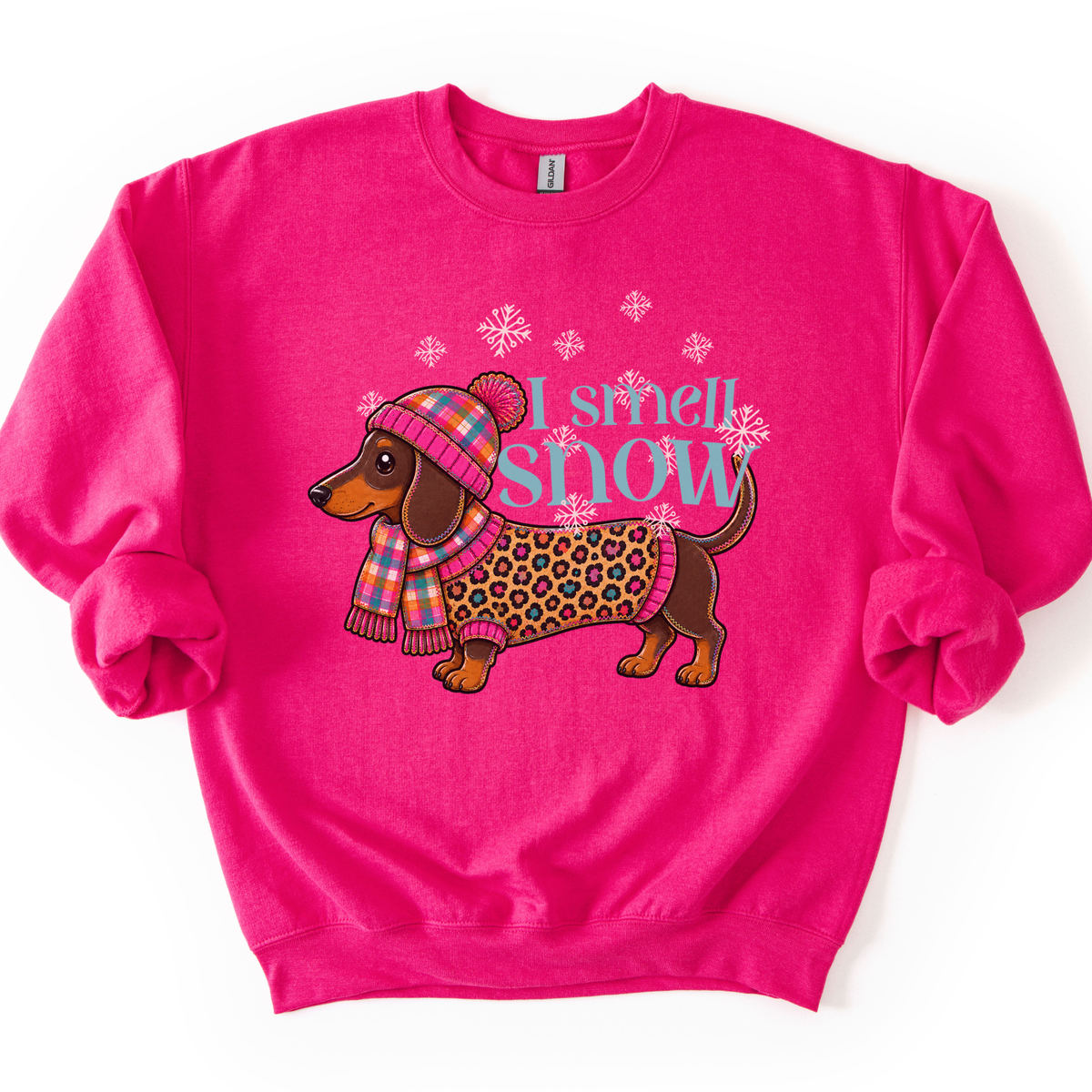 I smell snow featuring a dachshund dog bundled up in a sweater and hat with snowflakes around him.  On a pink heliconia sweatshirt