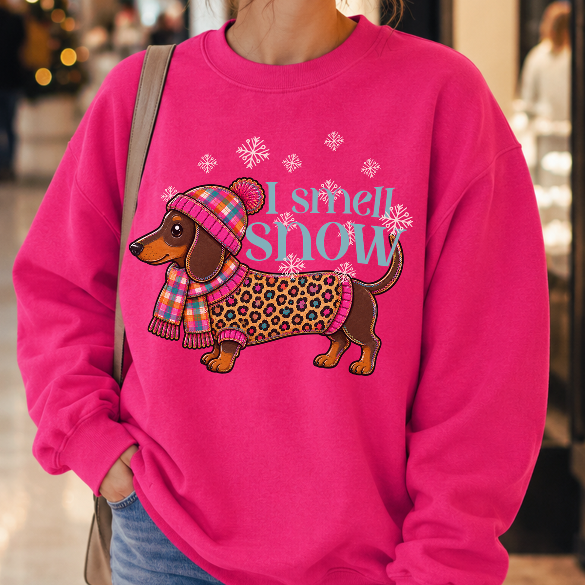 I smell snow featuring a dachshund dog bundled up in a sweater and hat with snowflakes around him.  On a pink heliconia sweatshirt