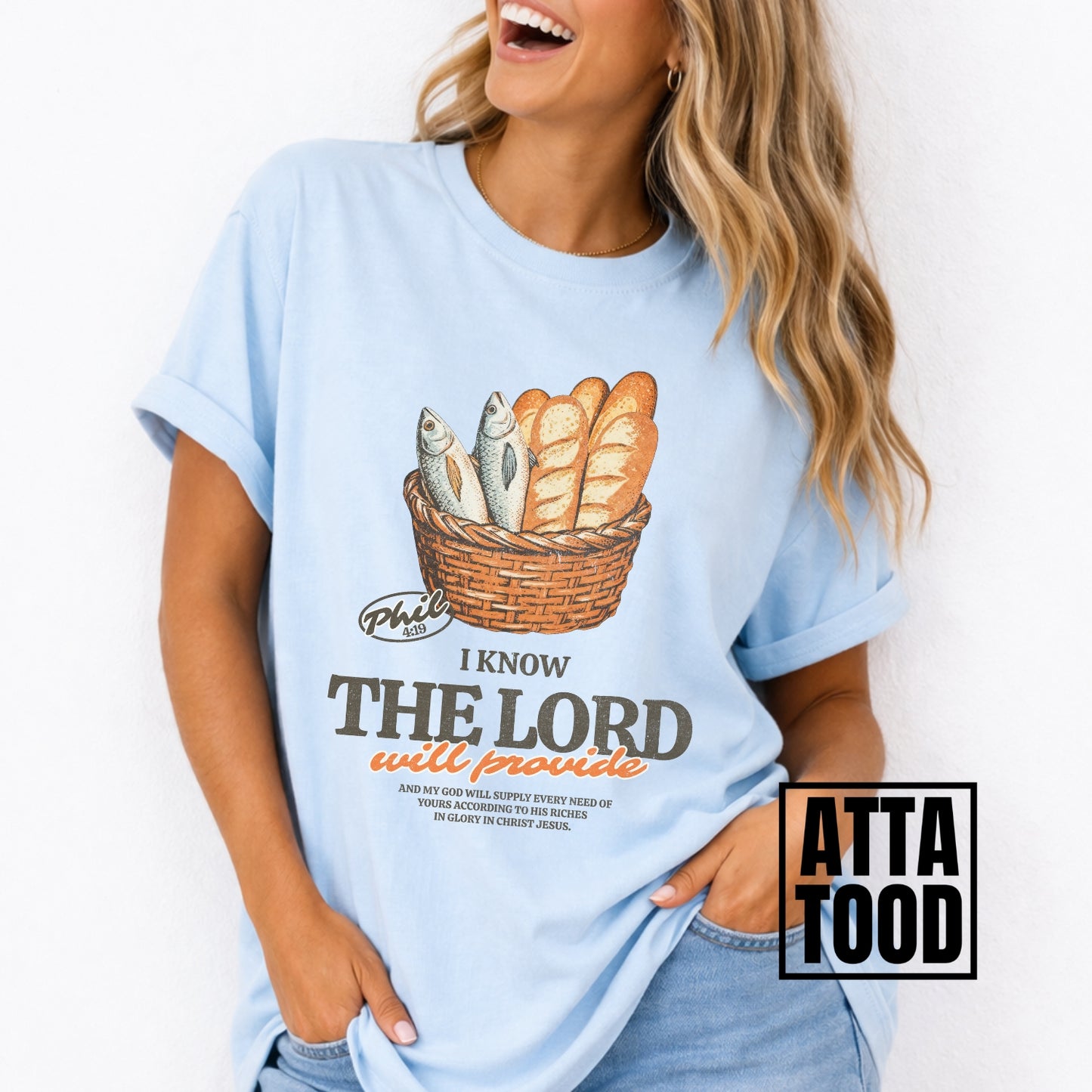 Person wearing a light blue t-shirt with a graphic design and text.  I know the Lord will provide featuring a basket of bread and fish referencing bible verse Philipians 4:19