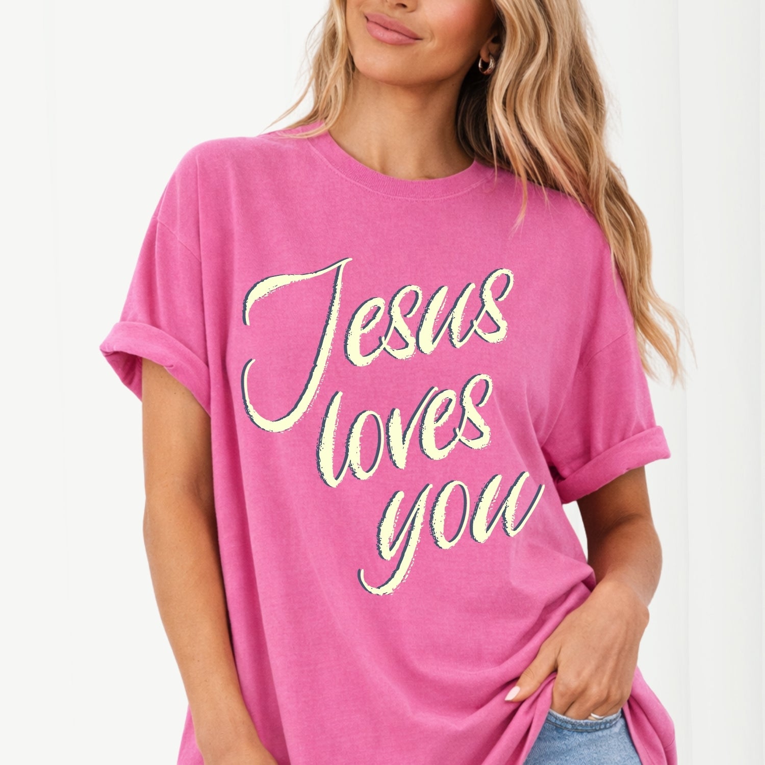 Person wearing a pink t-shirt with 'Jesus loves you' text on a plain background