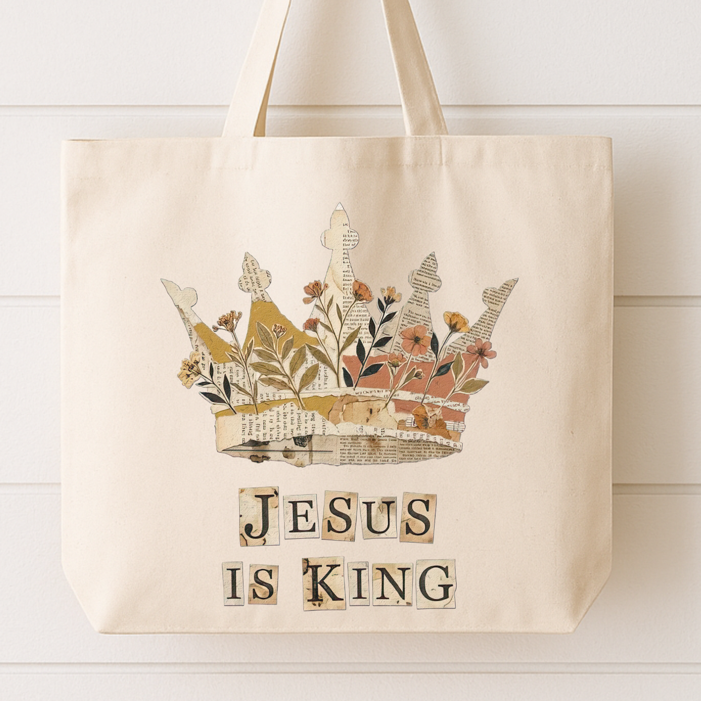 Beige tote bag with a floral crown design and 'Jesus is King' text on a white wooden surface.