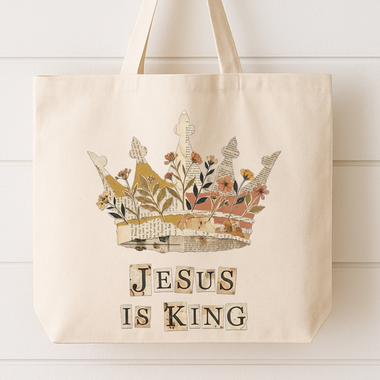 Beige tote bag with a floral crown design and 'Jesus is King' text on a white wooden surface.
