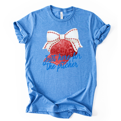 Blue t-shirt with a baseball and bow graphic and text on a white background.  the shirt says just here for the pitcher