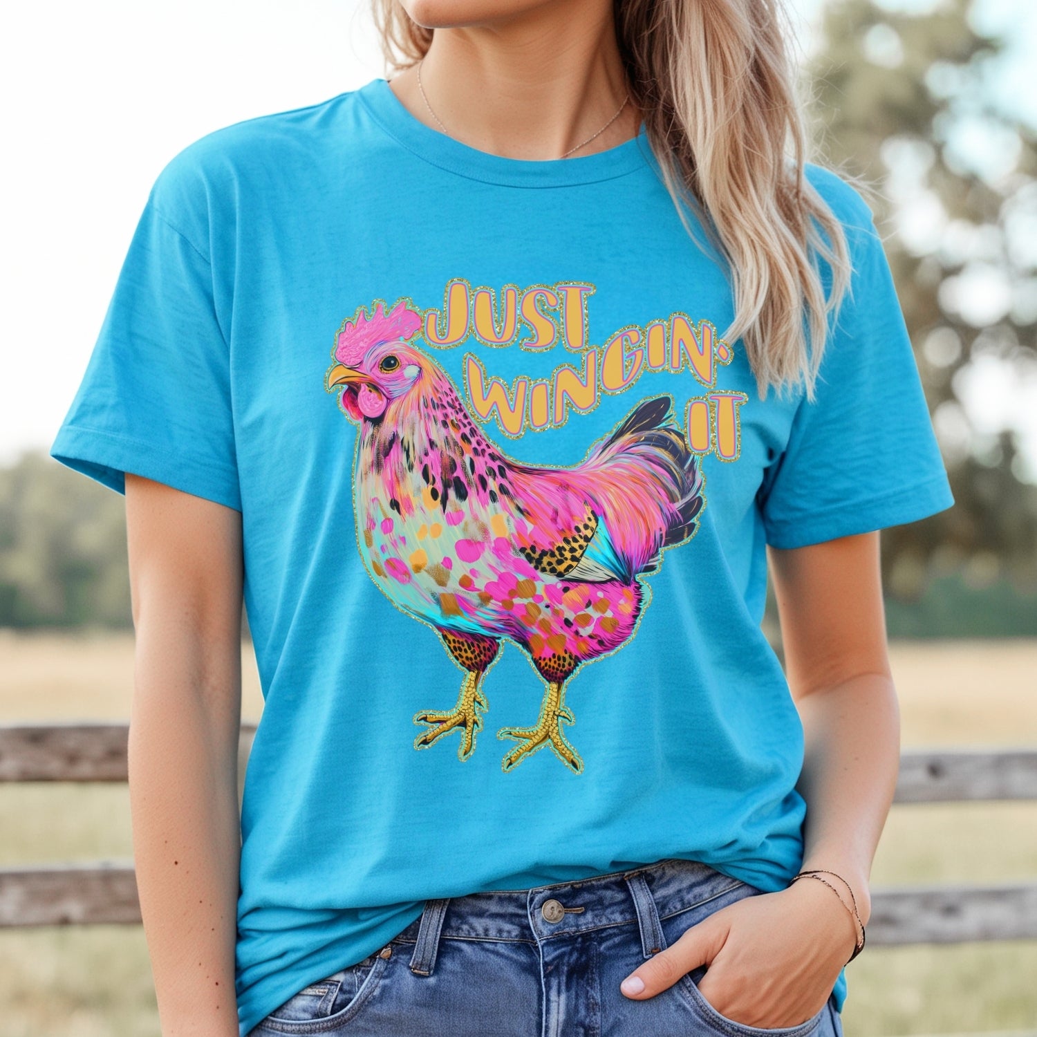 Person wearing a blue t-shirt with a colorful rooster graphic and text outdoors.