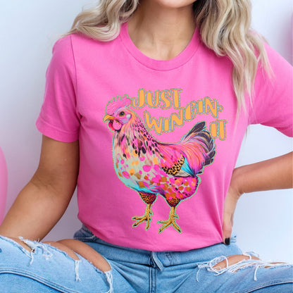 Person wearing a pink t-shirt with a colorful rooster graphic and text.
