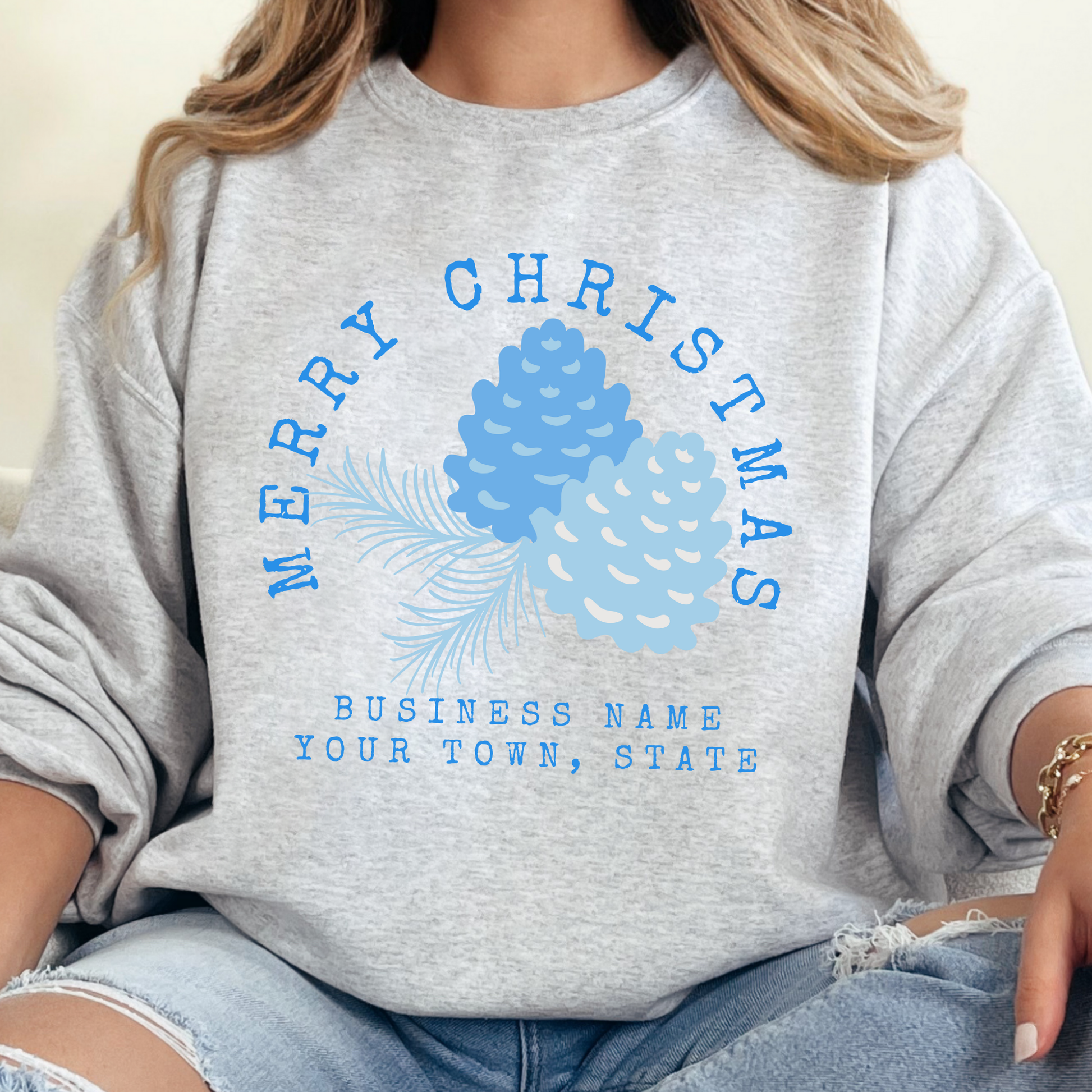 Ash sweatshirt that says Merry Christmas in blue and surrounding blue Christmas pinecones.  below you can customized the sweatshirt with your business name, town and state or both