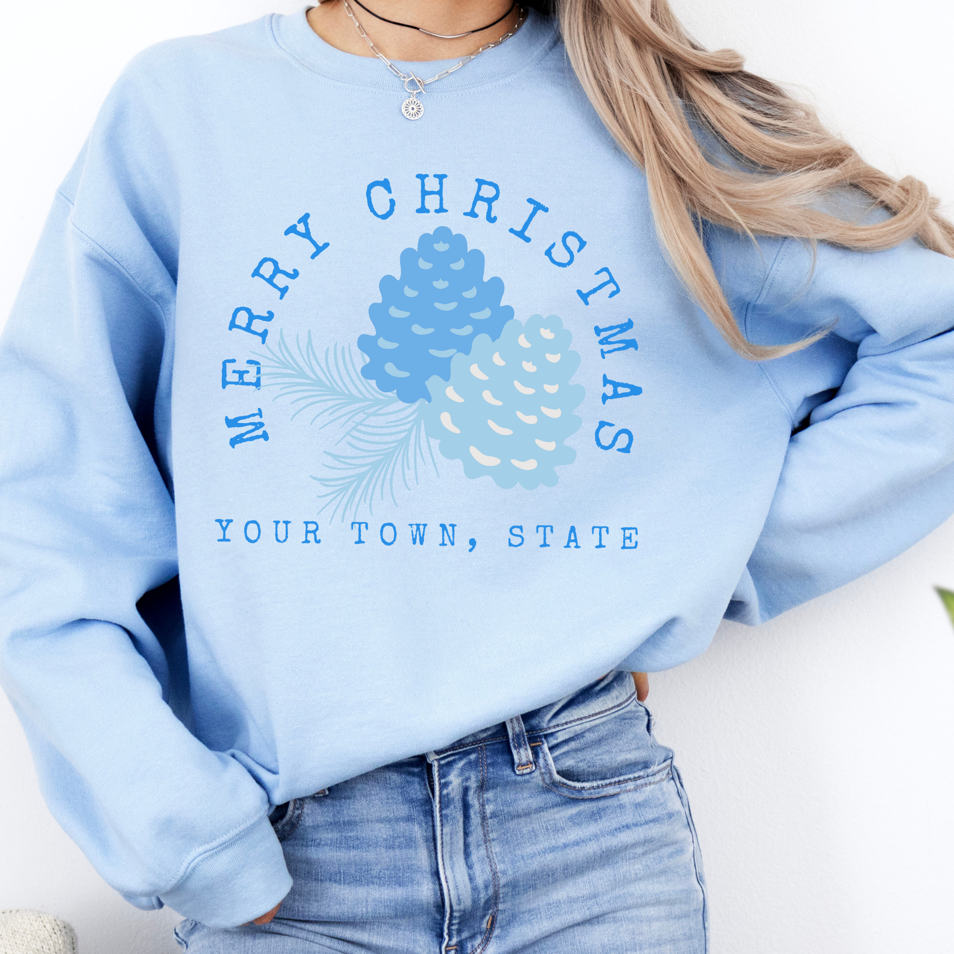 light blue sweatshirt that says Merry Christmas in blue and surrounding blue Christmas pinecones.  below you can customized the sweatshirt with your business name, town and state or both
