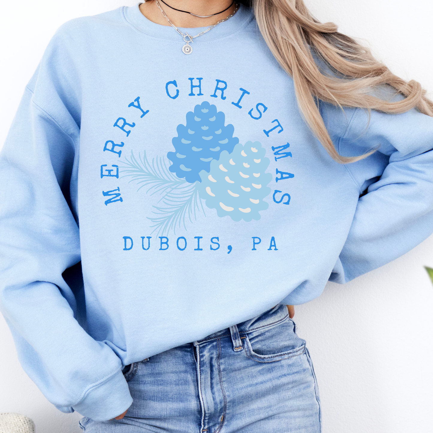 light blue sweatshirt that says Merry Christmas in blue and surrounding blue Christmas pinecones.  below you can customized the sweatshirt with your business name, town and state or both