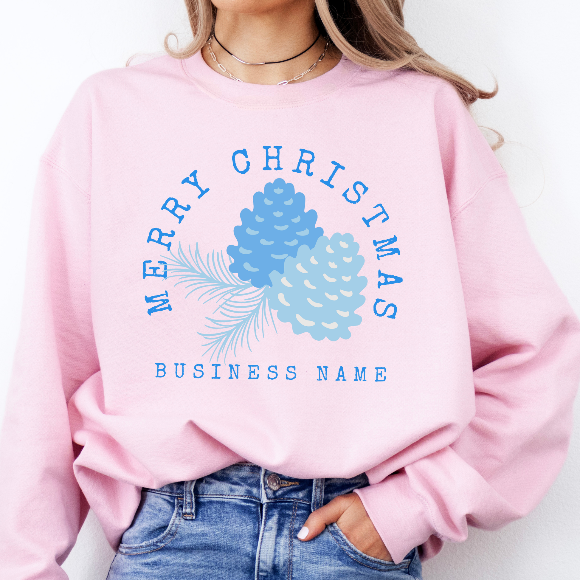 light pink sweatshirt that says Merry Christmas in blue and surrounding blue Christmas pinecones.  below you can customized the sweatshirt with your business name, town and state or both