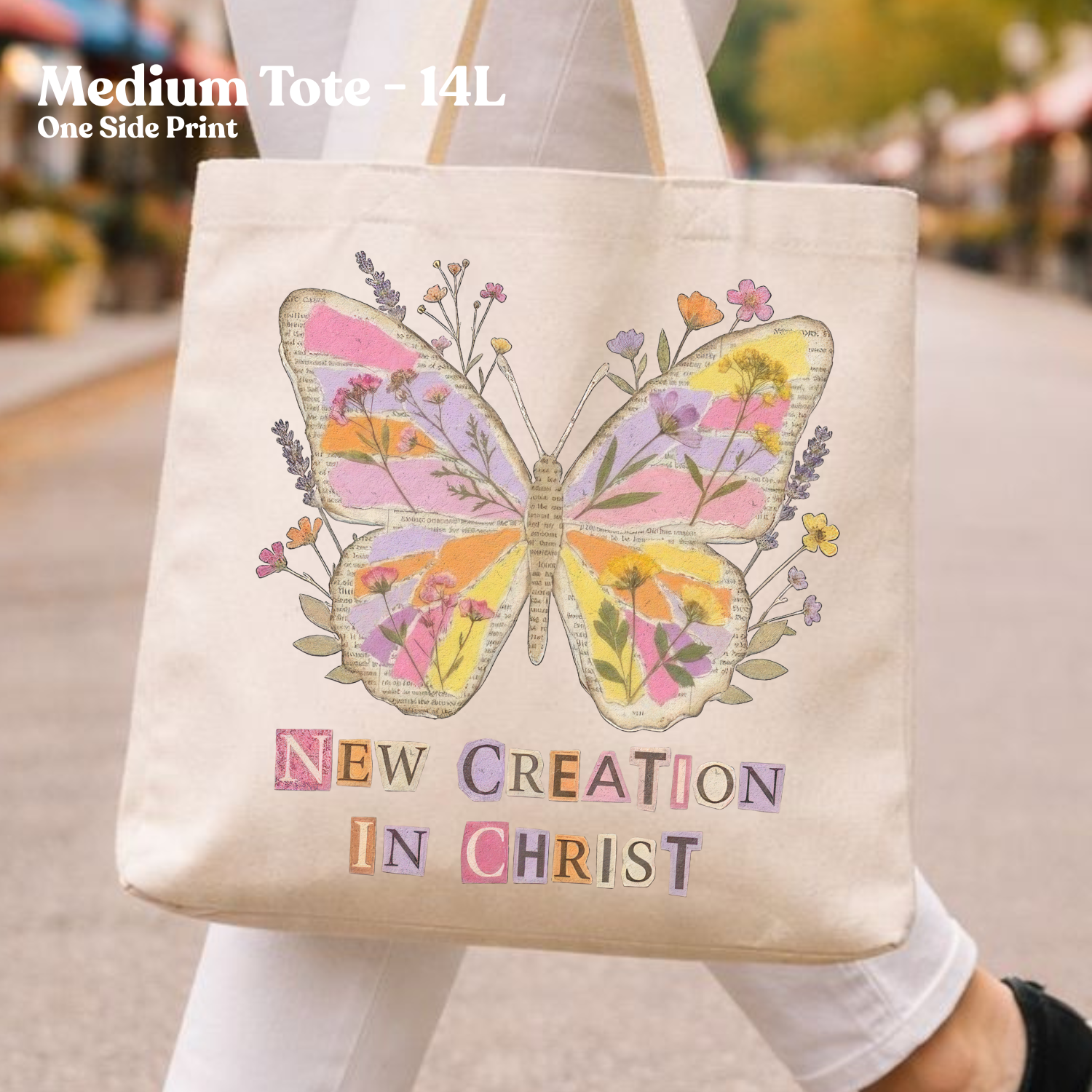 Tote bag with butterfly design and 'New Creation in Christ' text, held by a person outdoors.