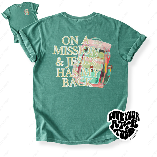Backpack graphic with faith message “On a Mission and Jesus Has My Back,” bold high-contrast painted-look artwork, printed on a Comfort Colors® garment-dyed tee.