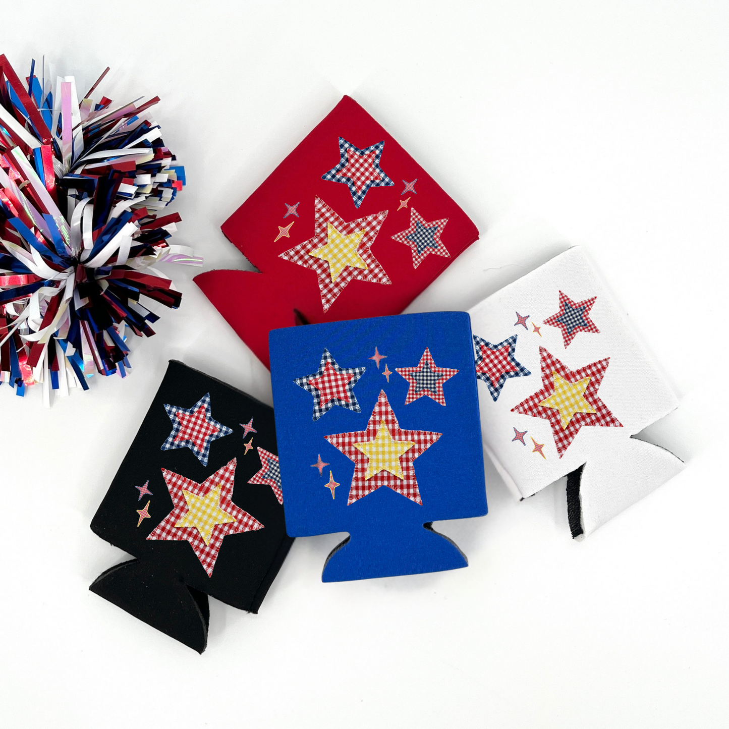 Red, Blue, Black and White collapsible can cooler displayed on a white background with a red, white, and blue metallic pom pom in the foreground. The graphic features red, white, and blue patchwork style stars with gingham patterns and small sparkles, creating a patriotic Americana star design printed on the front of the drink sleeve style can cooler.