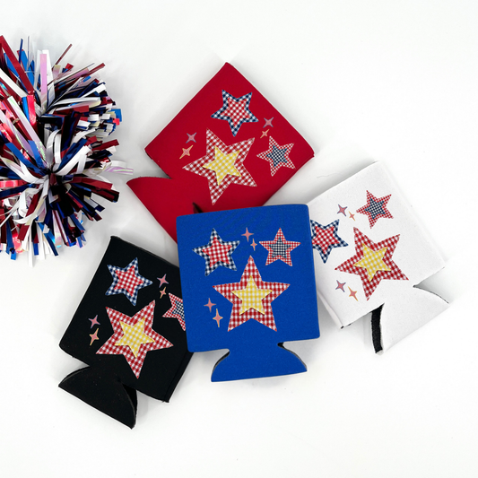 Red, Blue, Black and White collapsible can cooler displayed on a white background with a red, white, and blue metallic pom pom in the foreground. The graphic features red, white, and blue patchwork style stars with gingham patterns and small sparkles, creating a patriotic Americana star design printed on the front of the drink sleeve style can cooler.