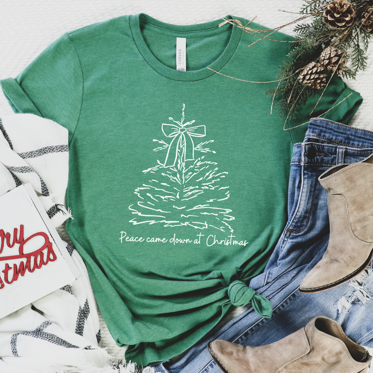 A simple faith-based Christmas design featuring a hand-drawn Christmas tree topped with a bow and the words “Peace Came Down at Christmas.” on a green tee