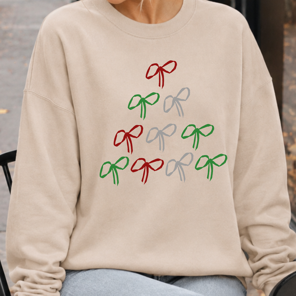 A simple Christmas tree made from hand-drawn bows in classic red, green, and silver on a sand color sweatshirt