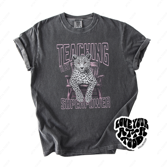 Leopard-print style graphic with teacher phrase “Teaching Is My Superpower,” high-contrast statement artwork with thick paint texture feel, printed on a Comfort Colors® tee.