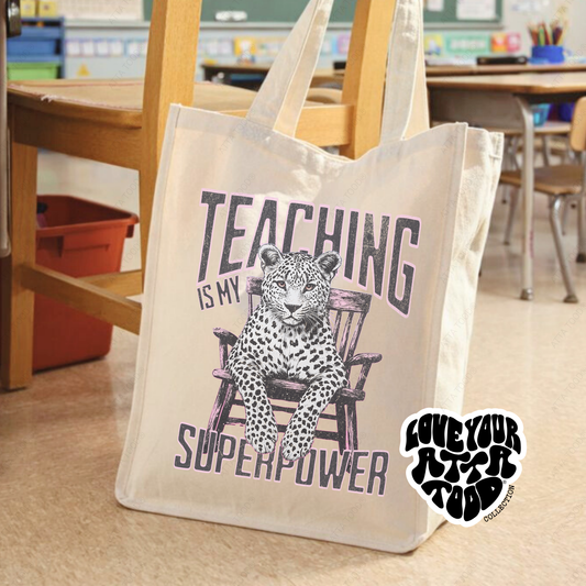 Jumbo canvas tote bag with teacher-themed “Teaching Is My Superpower” graphic, bold high-contrast painted-look artwork, Love your ATTA TOOD® brand mark, printed on both sides.