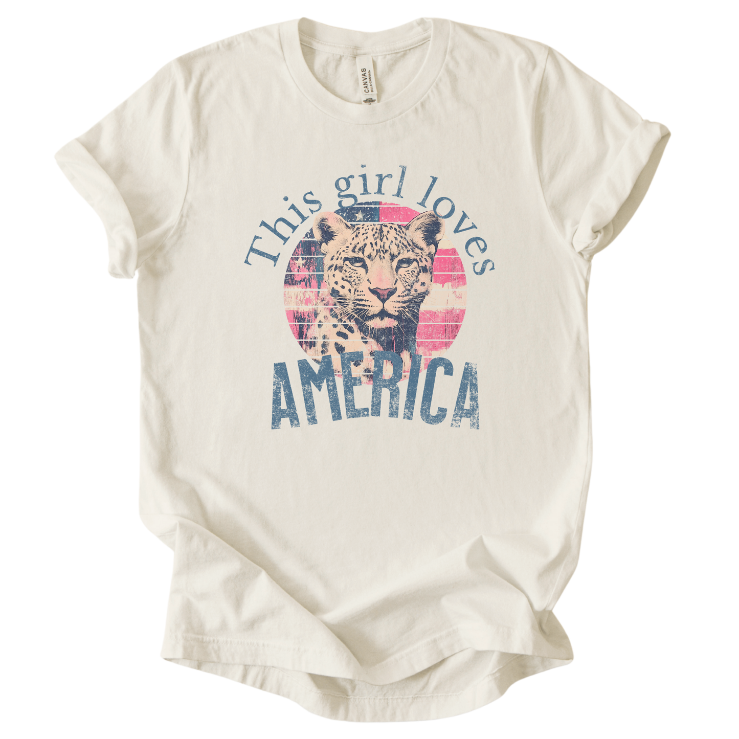 Patriotic Americana graphic on a beige t-shirt. The design features an illustrated leopard portrait centered over a distressed American flag circle, paired with the phrase “This Girl Loves America” in bold, vintage-style lettering. The worn texture and soft color palette create a modern patriotic look that blends animal imagery with classic Fourth of July appeal.