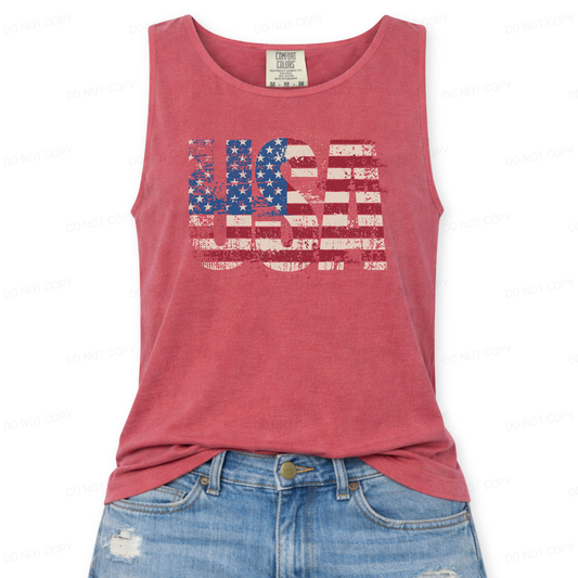 Distressed oversized "USA" overlayed with an American Flag on a Comfort Colors garment dyed unisex red tank top