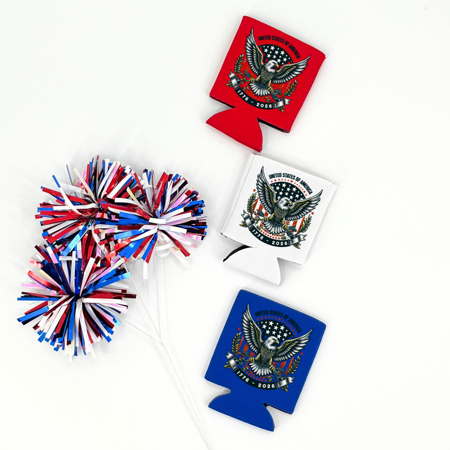 Assorted collapsible can coolers in red, white, and royal blue displayed with red, white, and blue metallic pom poms. The graphic features a bald eagle with patriotic stars and a crest reading “United States of America 1776–2026.” Patriotic design printed on the front of the drink sleeve style can coolers.