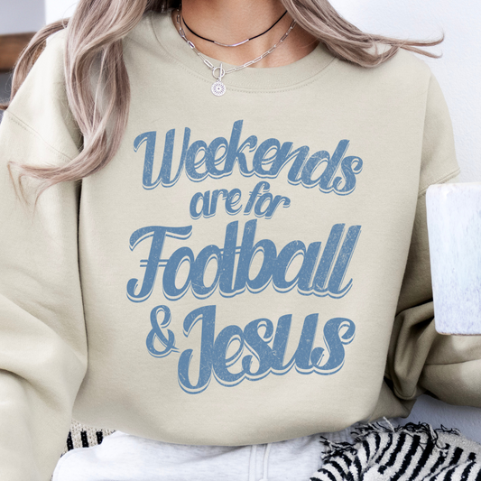 A woman wearing a beige sweatshirt with the text 'Weekends are for FOOTBALL & JESUS' printed on the front, holding a coffee cup, with a zebra-patterned blanket and a pendant visible in the background.