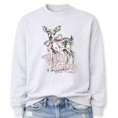 Ash gray  Bold Christian graphic on a Gildan crewneck sweatshirt. The design features a fawn with soft brown detailing and a large pink bow, paired with the phrase “Wildly Loved” in blush vintage-style lettering. 